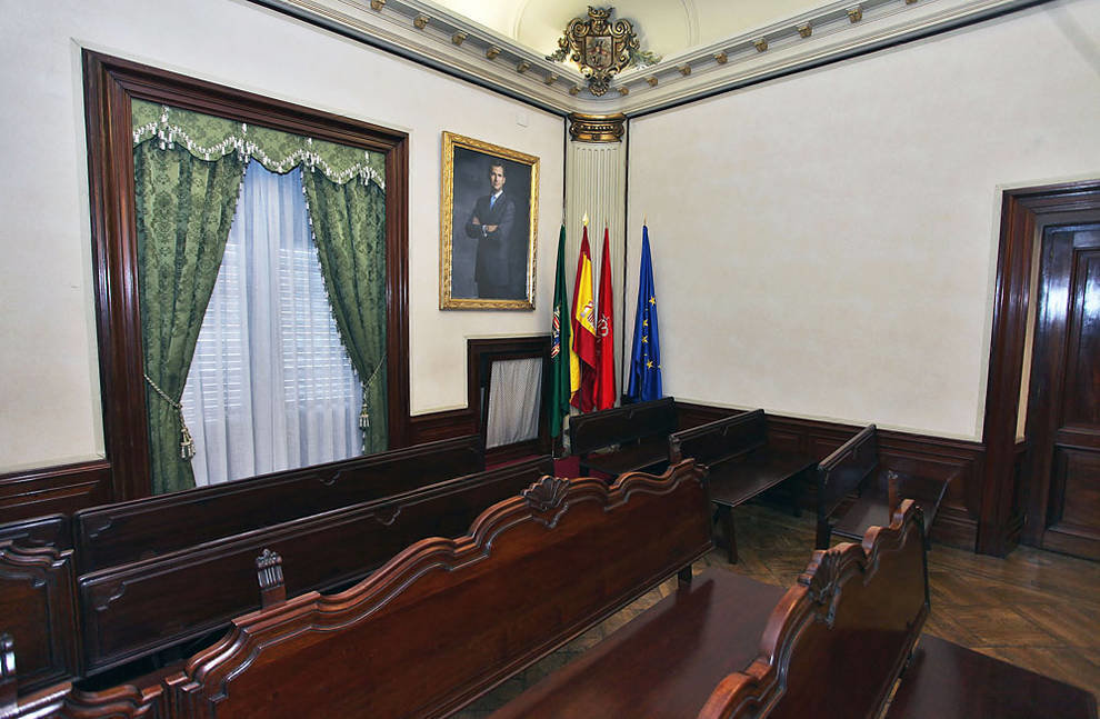 Retrato de Felipe VI y banderas, detrás del público del salón de plenos de Pamplona.