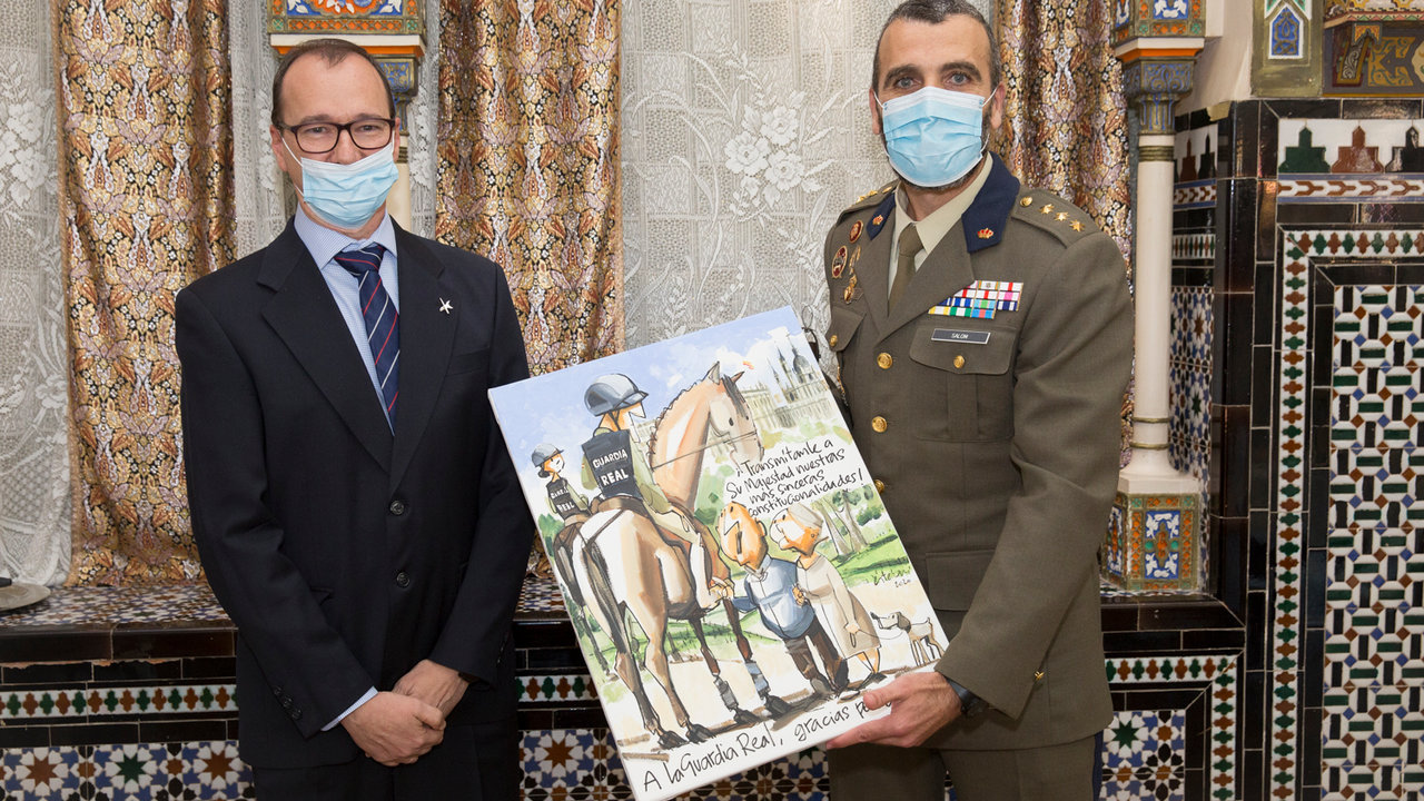El coronel jefe de la Guardia Real recibe de manos del humorista gráfico Esteban una de sus viñetas
